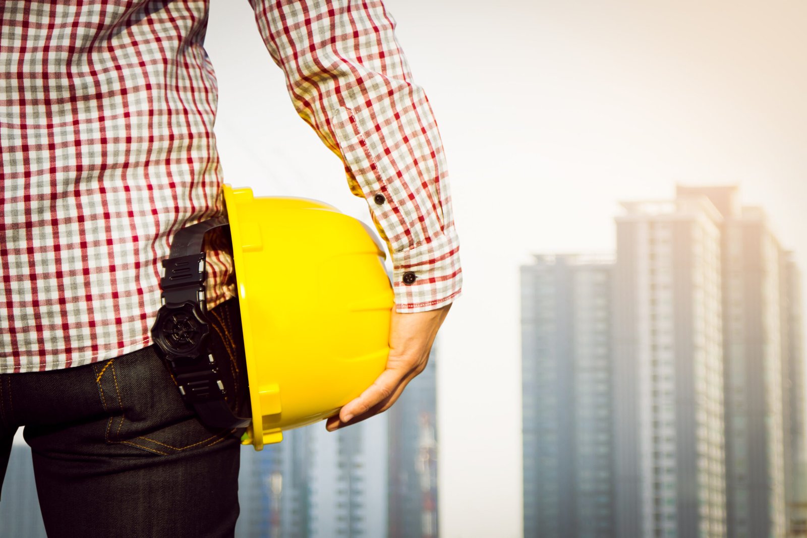 Hand's engineer worker holding yellow safety helmet with building on site background.